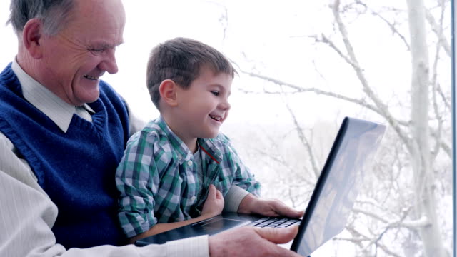 Junge-mit-Großvater-Lachen-mit-Laptop-zu-Hause-sitzen-zusammen