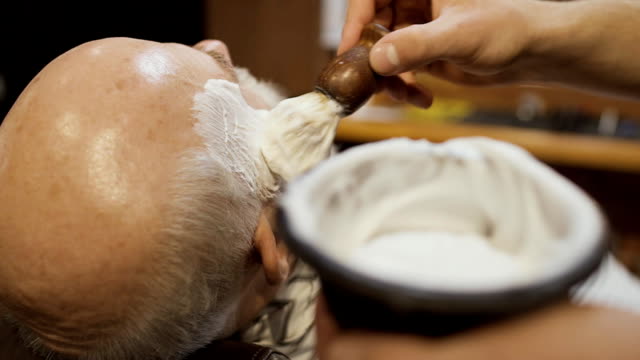 Barber-applies-shaving-cream-on-a-beard-of-mature-man