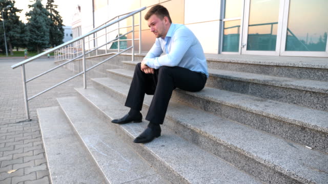 Close-up-of-upset-sad-manager-sitting-on-stairs-near-office-building-and-crying.-Desperate-young-businessman-got-a-very-bad-news-on-phone-and-feeling-despair-outdoor.-Concept-of-financial-crisis