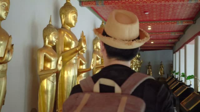 Jóvenes-asiáticos-viajan-a-turistas-de-mochila-caminar-dentro-en-Wat-Pho-templo-con-estatuas-de-Buda-dorado-en-la-fila-en-Bangkok,-Tailandia---viajes-mochila-explorar-ciudad-en-Asia