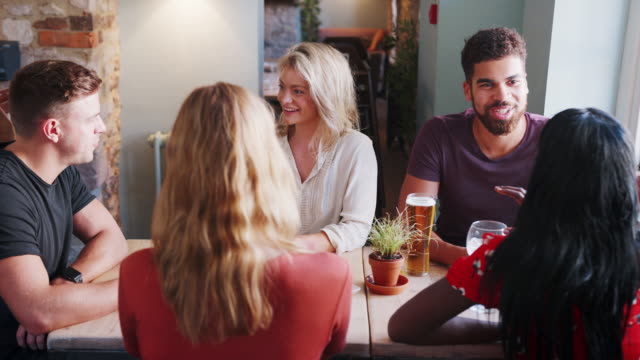 Mixed-race-group-of-young-adult-friends-sitting-at-a-table-in-a-pub-talking,-close-up