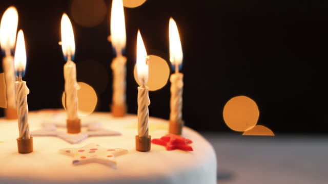 Nahaufnahme-von-brennenden-Kerzen-auf-einer-weißen,-verzierte-Geburtstagstorte-Bokeh-Lichter-im-Hintergrund