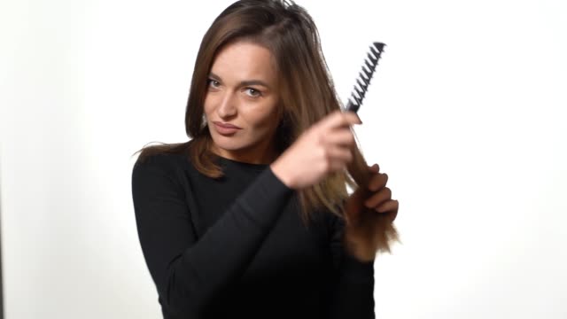 A-beautiful-woman-in-a-black-golf-is-combing-her-long-hair-on-a-white-background-in-the-studio.