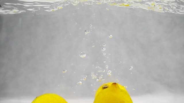 Three-yellow-lemons-simultaneously-fall-into-the-water-with-bubbles.-Video-in-slow-motion.