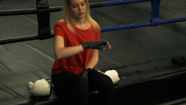 Das-Mädchen-die-Boxer-sitzt-in-einem-Ring-und-befasst-sich-mit-den-bandagierten-Händen