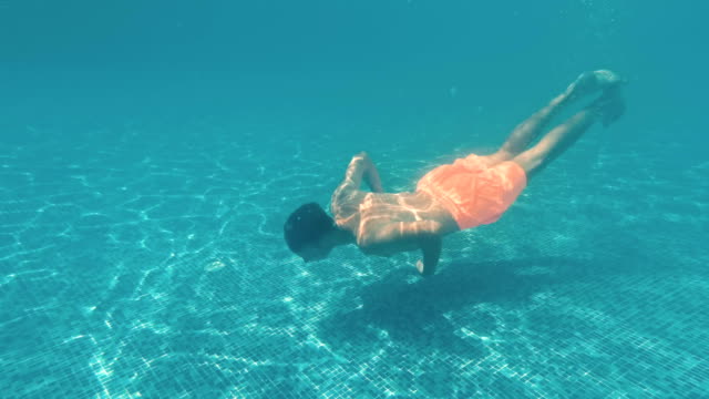 Chico-joven-nada-bajo-el-agua-en-una-piscina