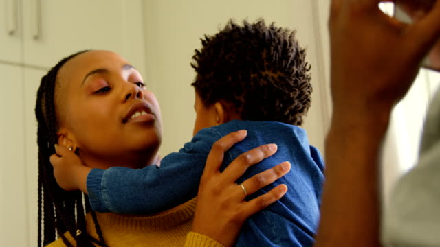 Vista-frontal-de-la-joven-madre-negra-sosteniendo-a-su-bebé-en-una-casa-confortable-4k