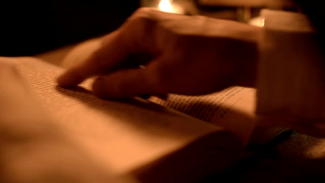 Big-Close-up-girl-magician-in-a-dark-room-with-candlelight-looking-for-a-spell-in-a-book.-Low-key-live-camera.
