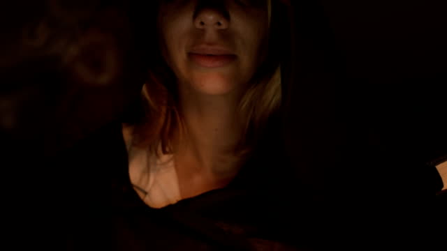Close-up-bottom-of-the-face-of-the-girl-magician-in-a-dark-room-with-candlelight-smiling-from-the-flash-below.-Low-key-live-camera
