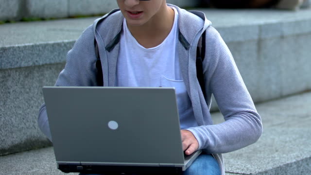 Young-male-working-on-laptop-outdoors,-it-genius-or-smart-teenage-hacker,-app