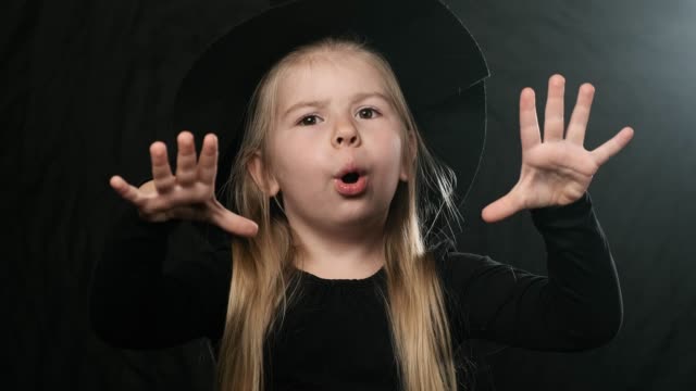 Halloween-witch-in-black-dress-and-hat-conjures.-Close-up-of-little-blonde-girl