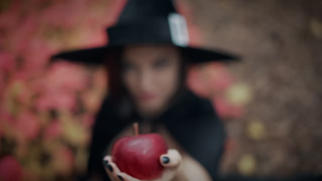 Mujer-como-bruja-de-negro-ofrece-manzana-roja-como-símbolo-de-tentación,-veneno.-Concepto-de-cuento-de-hadas,-Halloween,-cosplay.