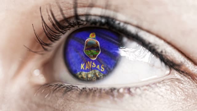 Mujer-ojo-verde-en-primer-plano-con-la-bandera-del-estado-de-Kansas-en-iris,-estados-unidos-de-América-con-movimiento-de-viento.-concepto-de-vídeo