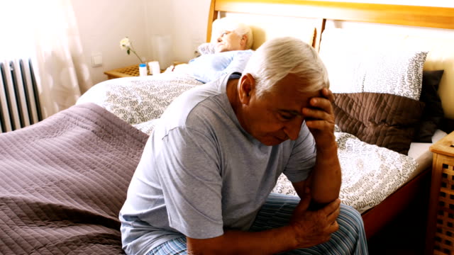 Tensed-senior-man-sitting-on-bed-in-bedroom