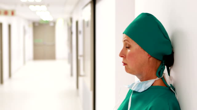 Tensed-female-surgeon-standing-in-corridor