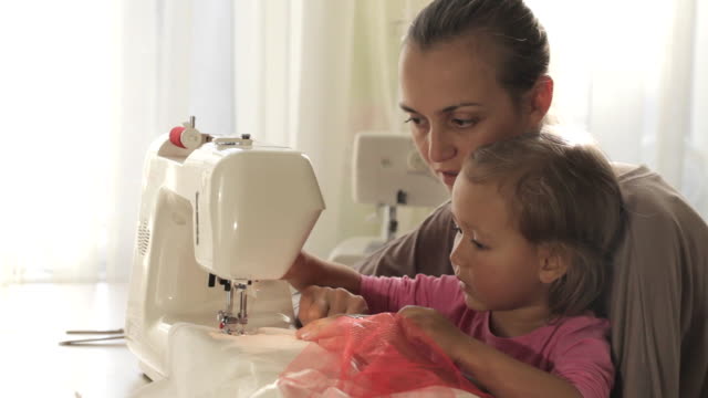 Attraktive-junge-Mutter-arbeitet-an-der-Nähmaschine-mit-ihr-kleine-süße-Tochter