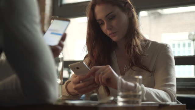 Woman-in-restaurant-reacts-to-a-funny-photo-on-phone-screen