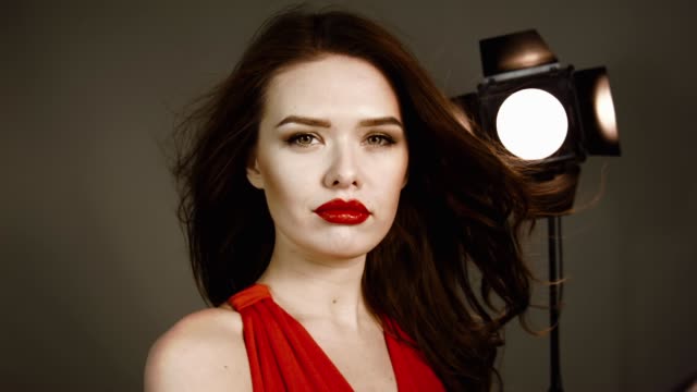 Girl-model-in-red-dress-with-red-lips-in-studio-posing-on-camera.