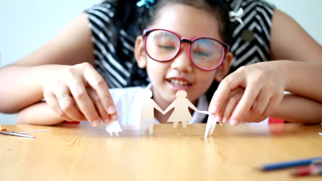 Niña-asiática-en-uniforme-de-estudiante-de-kindergarten-tailandés-usando-tijeras-para-cortar-el-papel-blanco-sobre-mesa-de-madera
