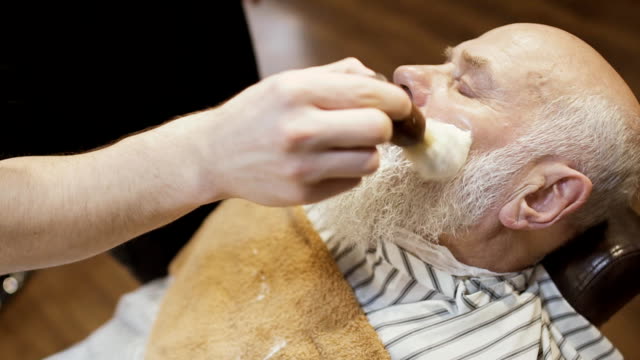 Barber-gilt-Rasierschaum-auf-Gesicht-des-älteren-Menschen