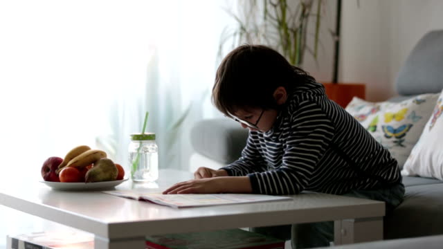 Preescolar-niño-con-gafas,-escribir-tareas-en-casa-en-el-soleado-salón