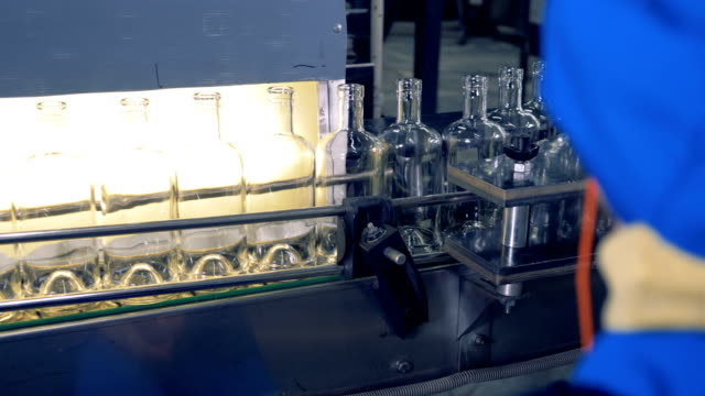 Empty-bottles-go-on-a-line,-while-a-factory-worker-watches-the-technology.-4K.