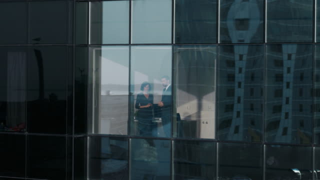 Luftaufnahmen-Footage-von-außerhalb-von-der-Wolkenkratzer:-Geschäftsmann-und-geschäftsfrau-sprechen-Unternehmen-stehen-durch-das-Bürofenster.-Schuss-von-der-finanziellen-Geschäftsviertel-und-Geschäftsleute-arbeiten-in-der-großen-Stadt-fliegen.