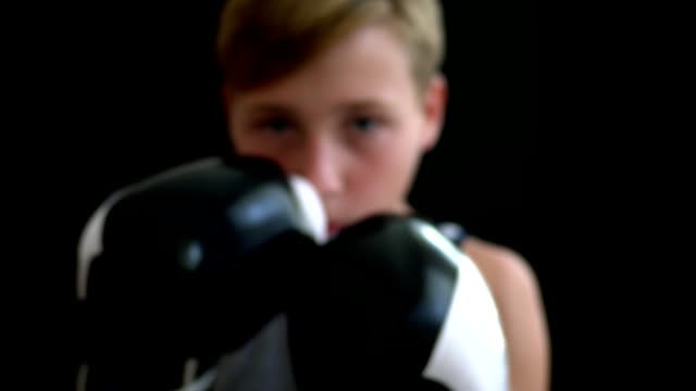 The-boy-is-engaged-in-boxing.-In-the-foreground-there-are-hands-in-black-and-white-gloves,-the-boy's-face-is-blurry.-A-boxer-in-a-gray-sports-shirt-stands-on-a-dark-background
