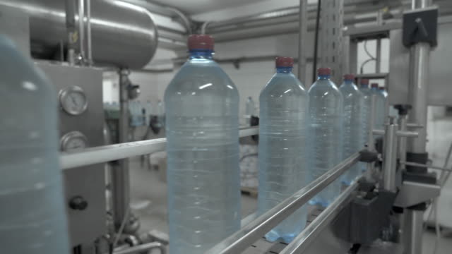Large-blue-plastic-bottles-filled-with-transparent-liquid-on-the-automatic-conveyor-line.-Close-up-of-water-bottling-line.