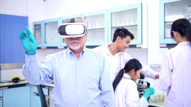 Scientists-working-in-lab-portrait.-Senior-chinese-male-scientist-working-in-lab-with-VR-head-set-pressing-the-button-portrait-with-his-team-in-background.-For-special-effect-overlay.