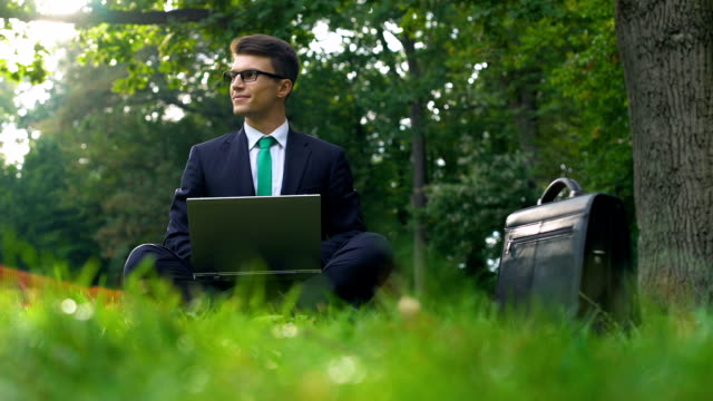 Business-man-sitting-on-grass-and-working-on-laptop-in-park-outside-office