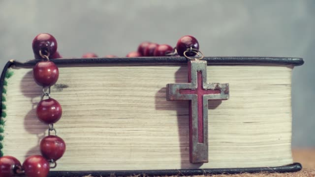 Open-Bible-and-the-crucifix-beads-on-a-golden-table,-close-up.-Beautiful-dark-background.-Religion-concept
