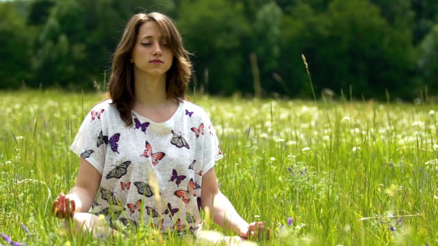 Meditación-al-aire-libre-en-campo-verde,-flor,-mujer-joven-se-sienta-en-posición-de-loto