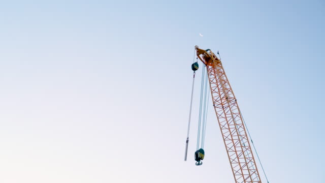 Construction-crane-gently-swaying-in-front-of-the-crescent-moon-at-twilight
