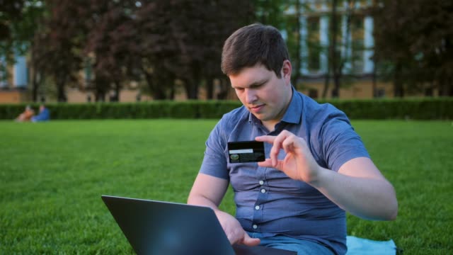 Mann-mit-Laptop-auf-dem-Rasen-im-Park-und-Kreditkarte