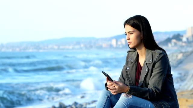 Comprobación-de-teléfono-adolescente-y-mirando-el-horizonte-en-la-playa