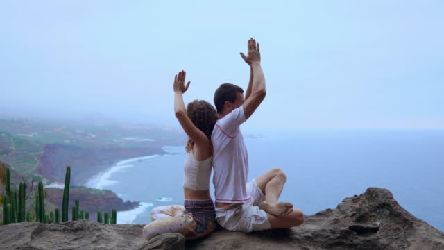 Mann-und-Frau-sitzen-auf-einem-Berg-auf-einem-Felsen-zurück-zu-meditieren-und-Yoga-auf-dem-Hintergrund-des-Ozeans-zu-tun.