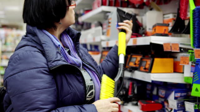 A-mature-woman-chooses-a-brush-with-scraper-in-the-supermarket.