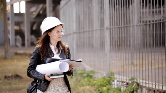 Student-girl-in-protective-helmet-and-goggles-and-inspects-the-construction-site,-using-the-technical-documentation