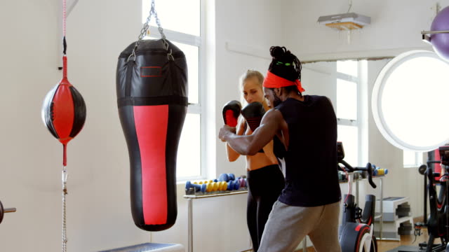 Trainer-assisting-female-boxer-in-fitness-studio-4k
