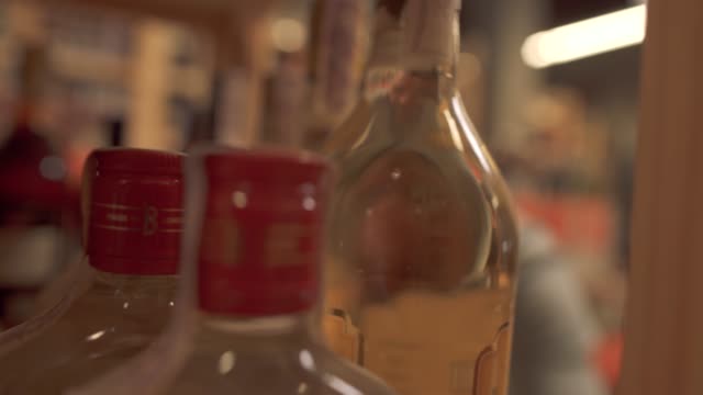 Guy-taking-a-bottle-of-alcoholic-beverage-from-a-wooden-shelf-in-liquor-store.-Man-is-out-of-focus.