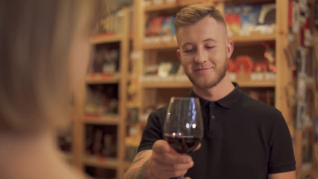 Male-visitor-to-a-liquor-store-takes-the-offered-wine-glass-and-sniffs-the-aroma-of-the-wine.-The-focus-moves-from-girl-to-boy.