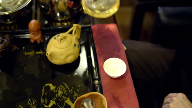 Tee-Zeremonie.-Master-gießt-in-eine-weiße-Tasse-grüner-Tee-aus-einer-Glas-Teekanne