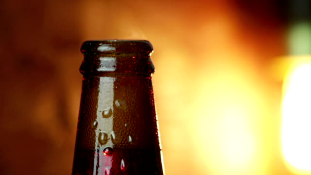 Mann-entkorken-eine-Flasche-Bier-mit-Schaum-mit-Eis-gefrorenen-Tropfen-auf-gold-braune-Hintergrund,-Spaß-und-Ernährung-trinken