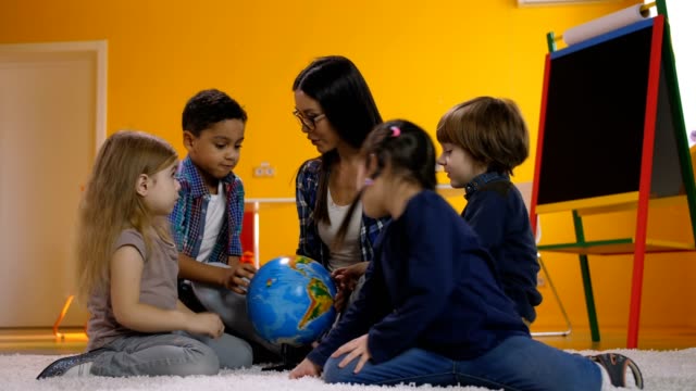Teacher-and-kids-discussing-globe-in-kindergarten