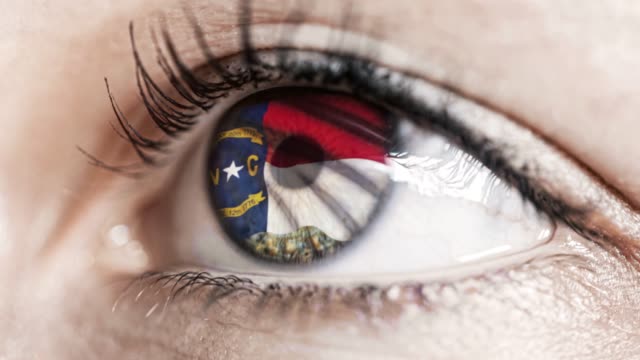 Mujer-ojo-verde-en-primer-plano-con-la-bandera-del-estado-de-Carolina-del-Norte-en-iris,-estados-unidos-de-América-con-movimiento-de-viento.-concepto-de-vídeo