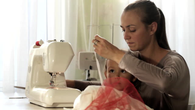 Attraktive-junge-Mutter-arbeitet-an-der-Nähmaschine-mit-ihr-kleine-süße-Tochter