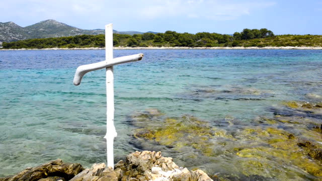 Wooden-christian-white-cross-on-rocky-shore-of-blue-sea.-Seacoast-of-Hvar-island-and-harbour-in-old-town-Hvar.