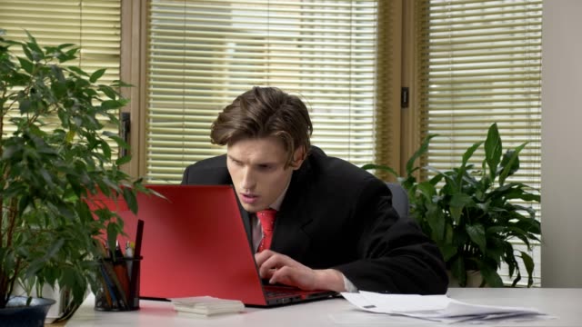Young-guy-in-a-suit-is-sitting-at-the-office,-working-on-a-laptop,-tired,-falling-asleep,-bored.-60-fps