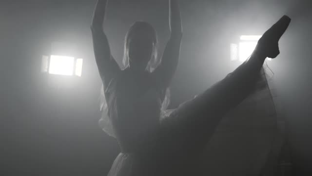 Professional-ballerina-dancing-ballet-in-spotlights-on-big-stage.-Beautiful-caucasian-young-girl-wearing-white-tutu-dress.-Black-white-vintage-retro-effect-tonned.-Slow-motion